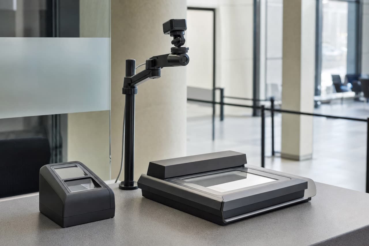 A biometric enrolment station on a civic office counter: fingerprint scanner, document reader and camera.