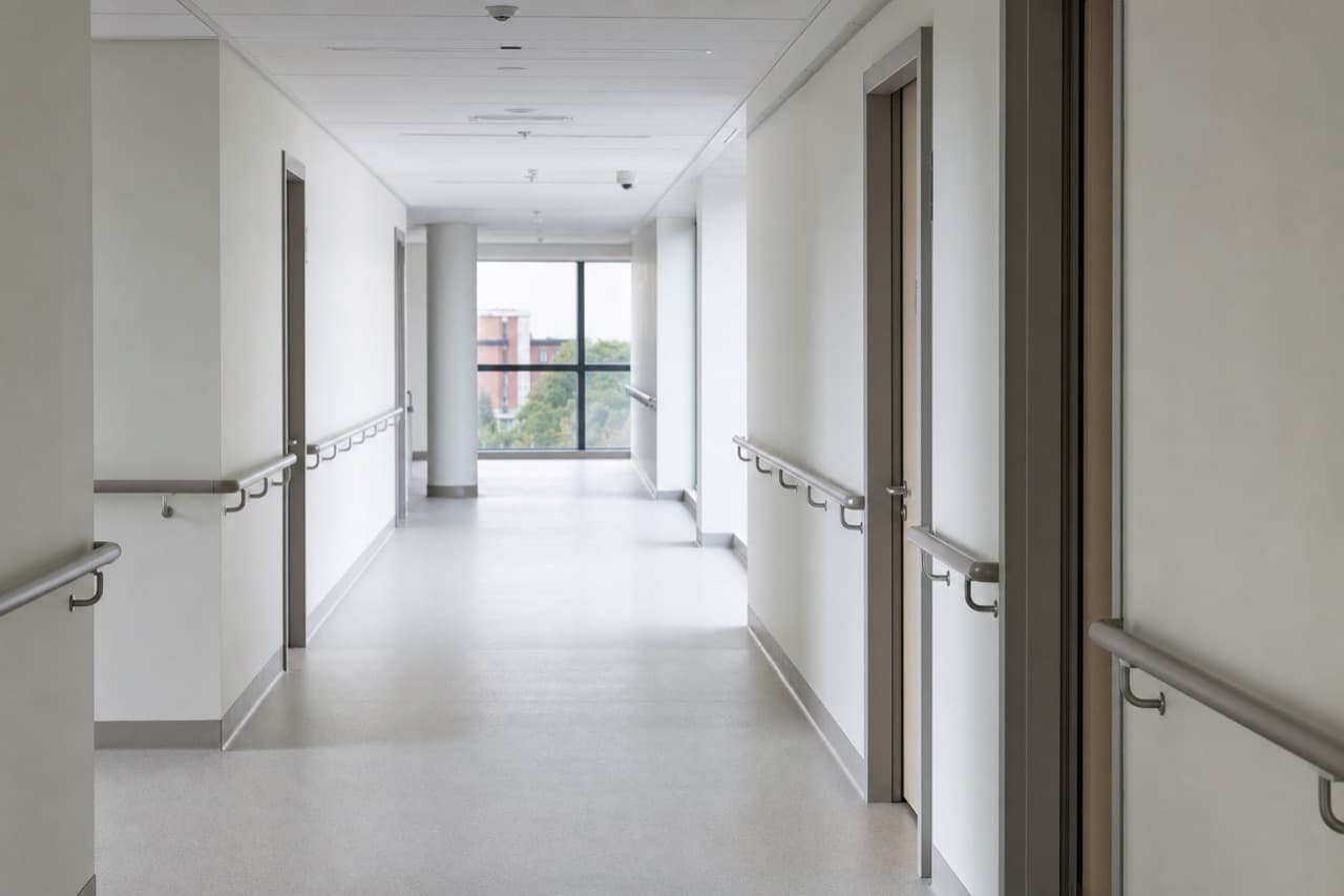 An empty corridor in a newly built hospital wing, daylight from the far window.