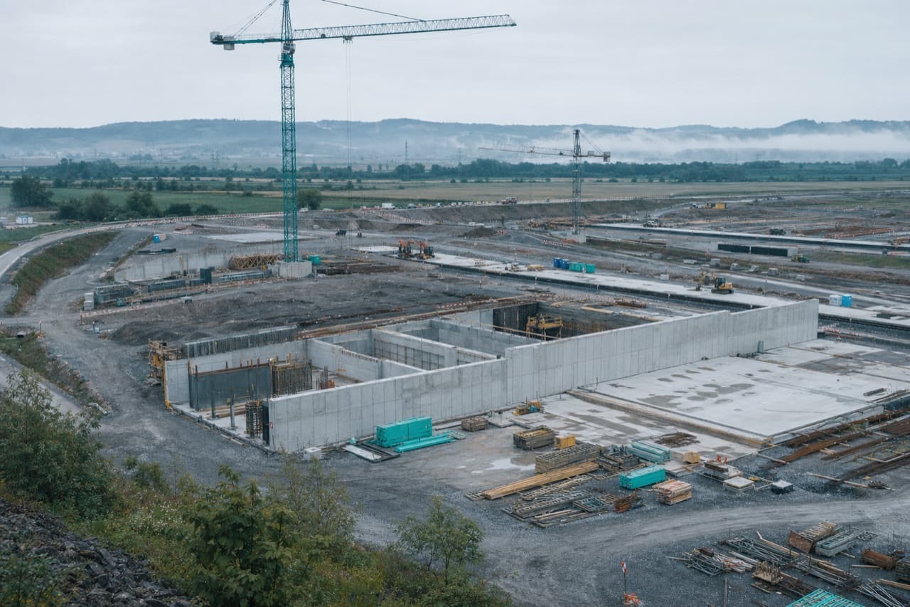 A large civil infrastructure site at first light: tower cranes, concrete forms and laid-out roadways.