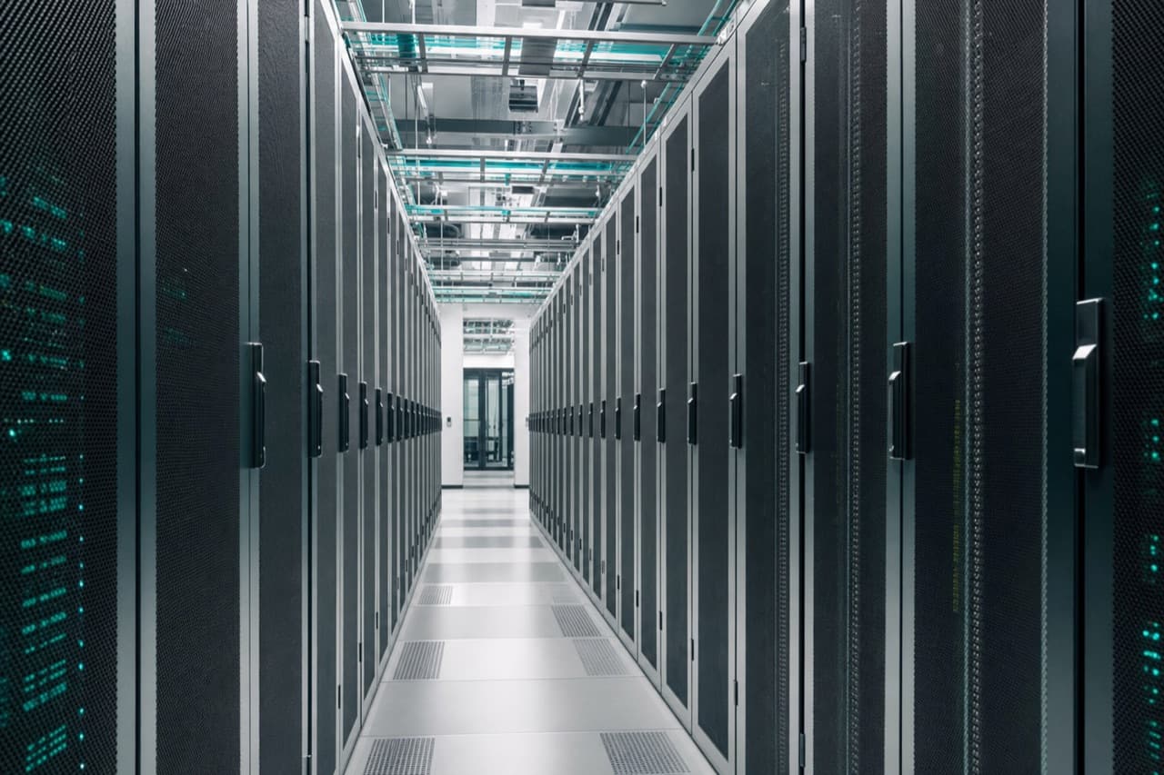 A corridor of server cabinets inside a data centre, receding under even lighting.