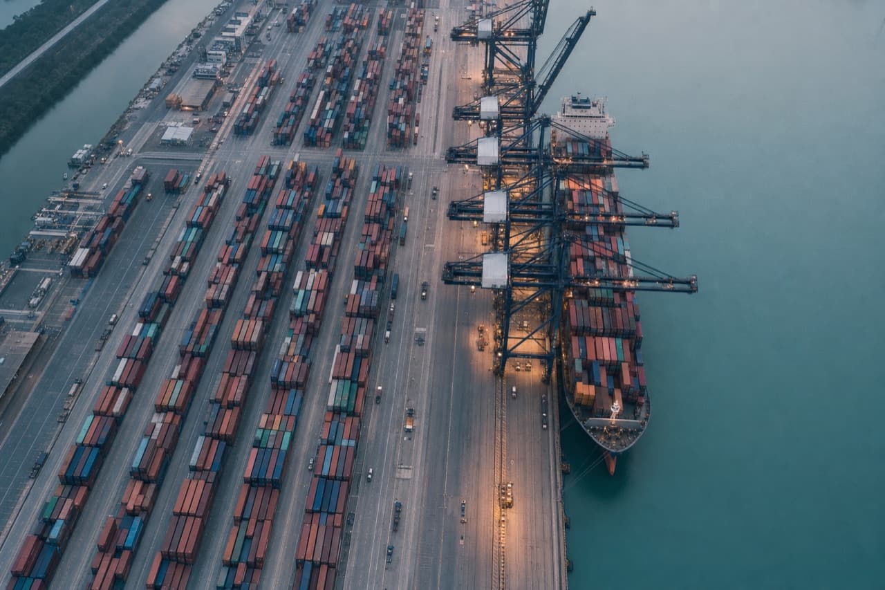 A container port at dawn seen from above: rows of stacked containers, gantry cranes along the quay.