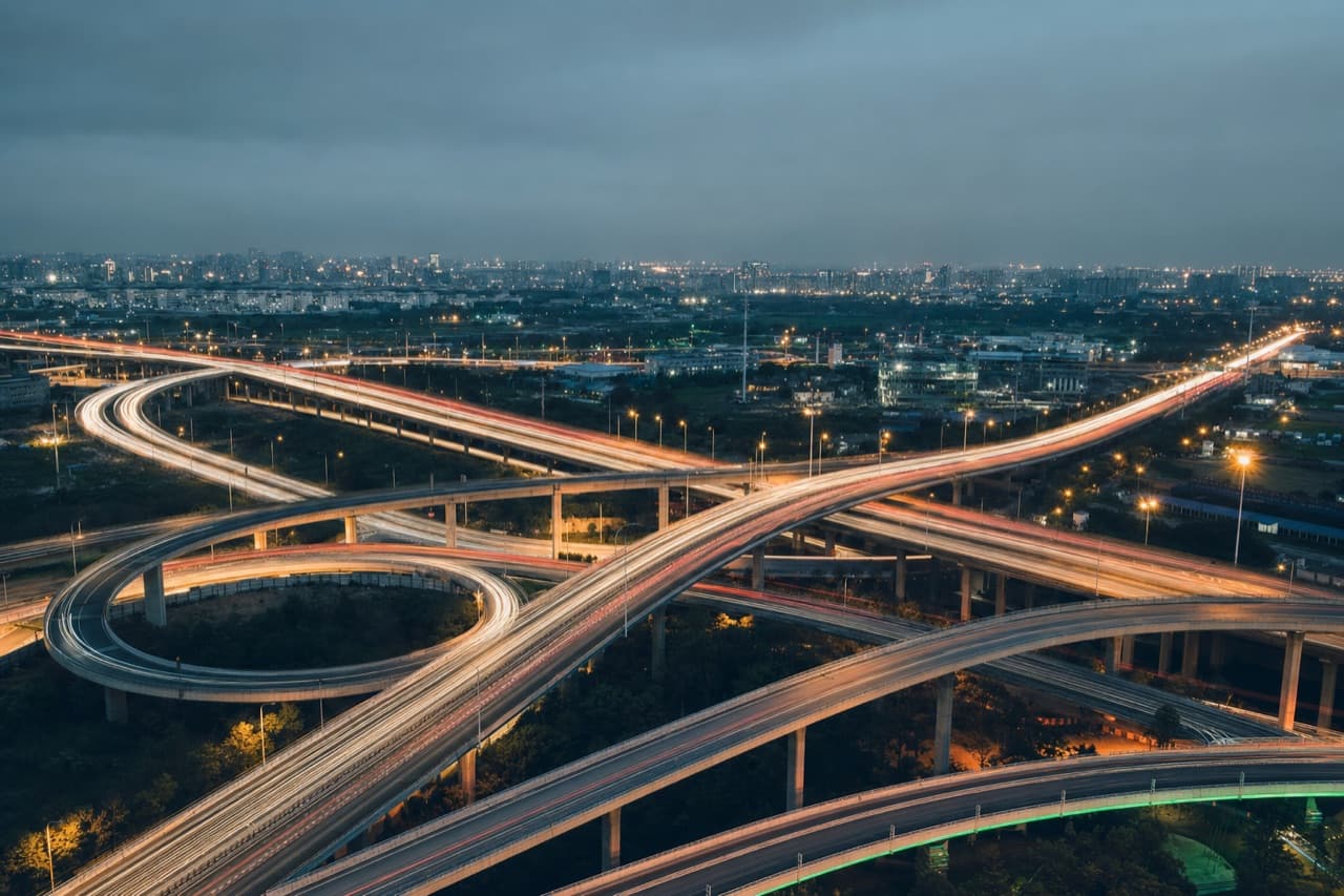 A multi-level road interchange at night, traffic drawn out into ribbons of light.